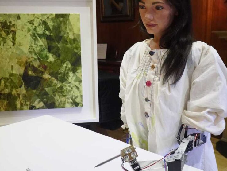Foto de Ai-Da, el robot pintor, con una pintura en el fondo